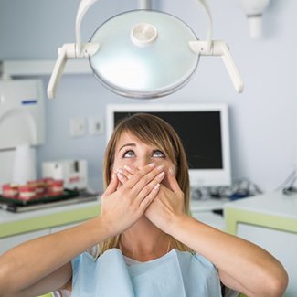 Young woman covering her mouth in fear in the dental chair