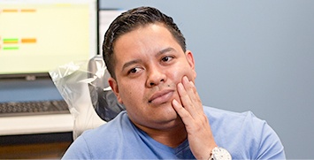 Male dental patient in dental chair holding his cheek in pain