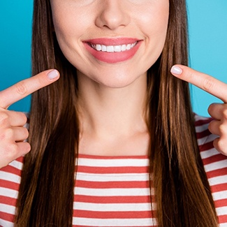 Young woman pointing toward her mouth to show off her new veneers